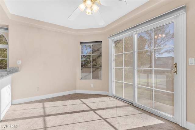 interior space featuring a tray ceiling, light tile patterned floors, a ceiling fan, and baseboards