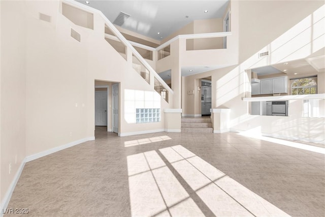 unfurnished living room with visible vents, a high ceiling, and baseboards