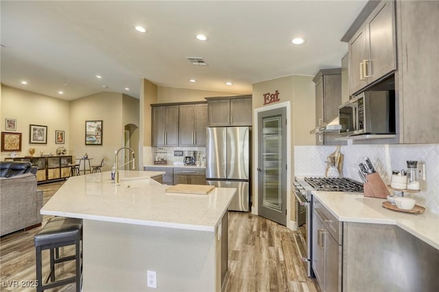 kitchen with open floor plan, lofted ceiling, appliances with stainless steel finishes, arched walkways, and a sink