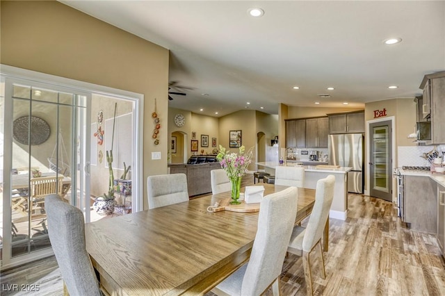 dining space with light wood-type flooring, a ceiling fan, recessed lighting, arched walkways, and lofted ceiling