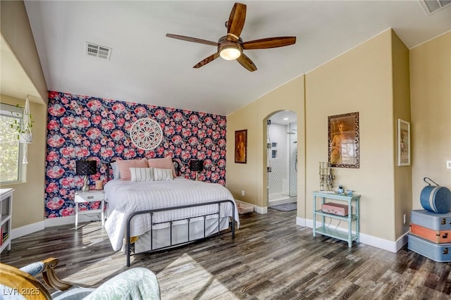 bedroom featuring wood finished floors, visible vents, baseboards, arched walkways, and an accent wall