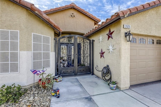 entrance to property with a tile roof, a gate, and stucco siding