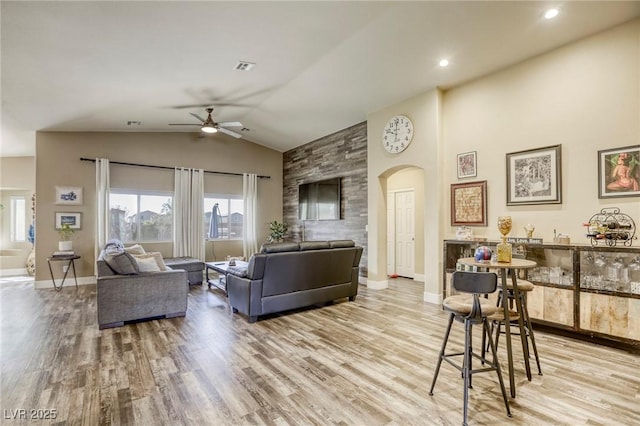 living room featuring wood finished floors, baseboards, arched walkways, ceiling fan, and vaulted ceiling