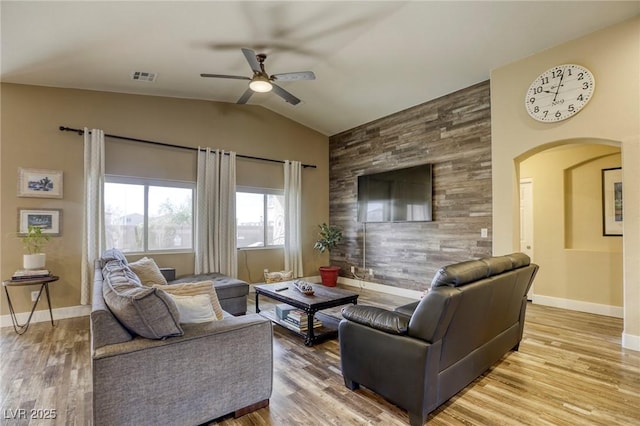 living room featuring visible vents, a ceiling fan, arched walkways, lofted ceiling, and an accent wall