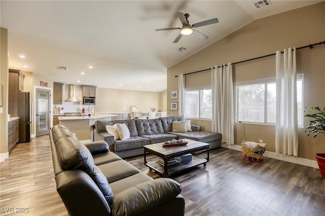 living room featuring a ceiling fan, lofted ceiling, light wood-style floors, and visible vents