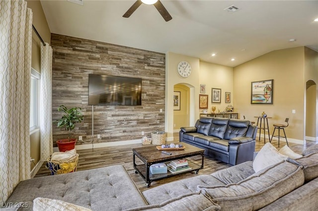 living room with arched walkways, visible vents, an accent wall, and a ceiling fan