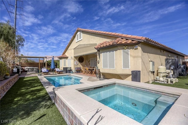 rear view of property with a tiled roof, stucco siding, a lawn, an in ground hot tub, and a patio