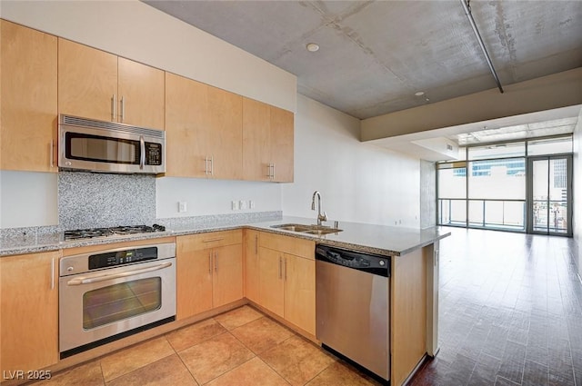 kitchen with light brown cabinetry, a sink, open floor plan, appliances with stainless steel finishes, and a peninsula