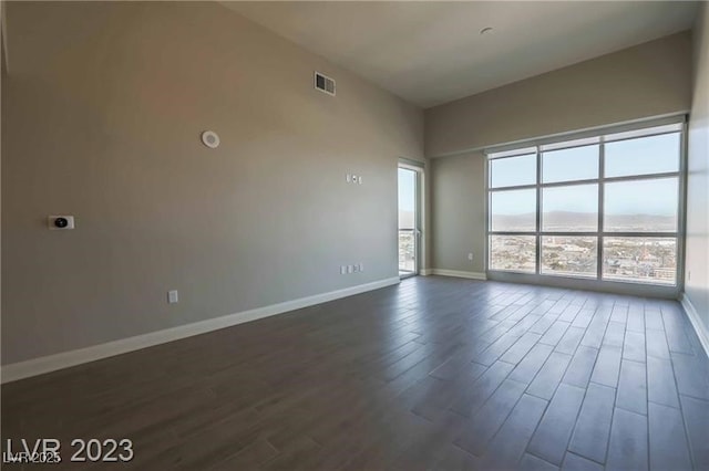 spare room with a towering ceiling, baseboards, visible vents, and dark wood-style flooring