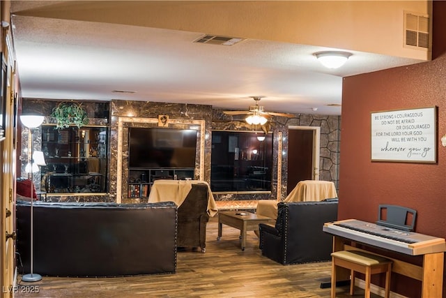 living area featuring a textured wall, visible vents, a ceiling fan, and wood finished floors