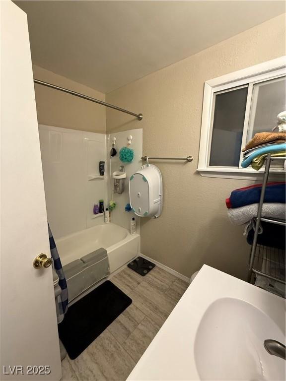 1016 Park Ave, Ely, NV 89301 - bathroom with a textured wall, baseboards, a sink, washtub / shower combination, and wood finished floors