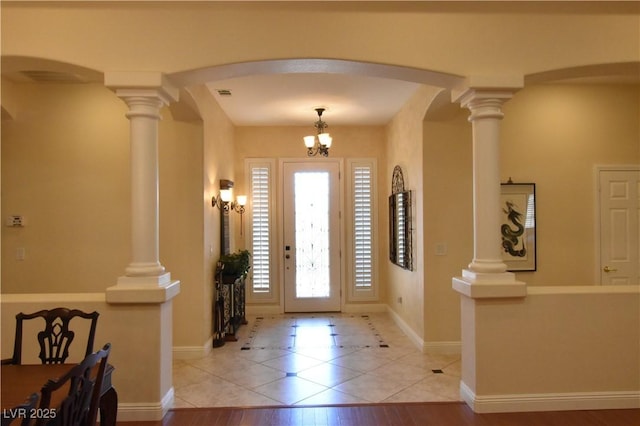 foyer entrance with arched walkways, light tile patterned floors, decorative columns, baseboards, and a chandelier