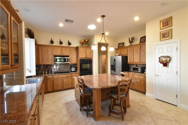 kitchen featuring black appliances, a sink, light stone counters, a center island, and decorative backsplash