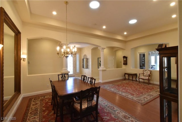 dining area with an inviting chandelier, a raised ceiling, wood finished floors, and arched walkways