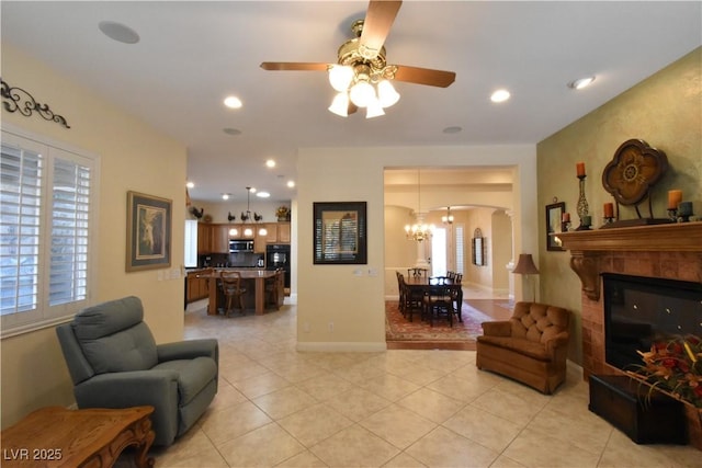 living area with baseboards, light tile patterned flooring, recessed lighting, arched walkways, and ceiling fan with notable chandelier