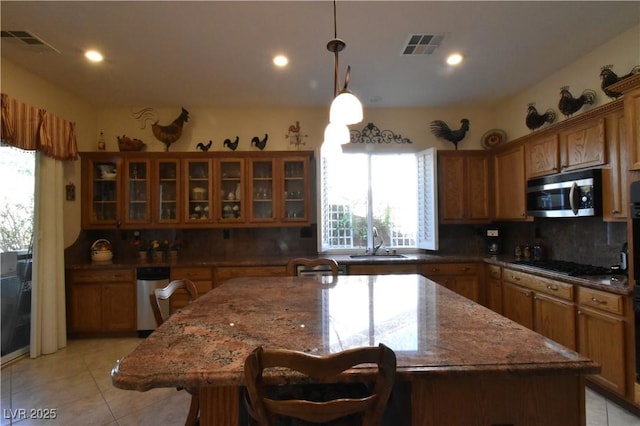 kitchen with gas cooktop, brown cabinetry, a sink, decorative backsplash, and stainless steel microwave