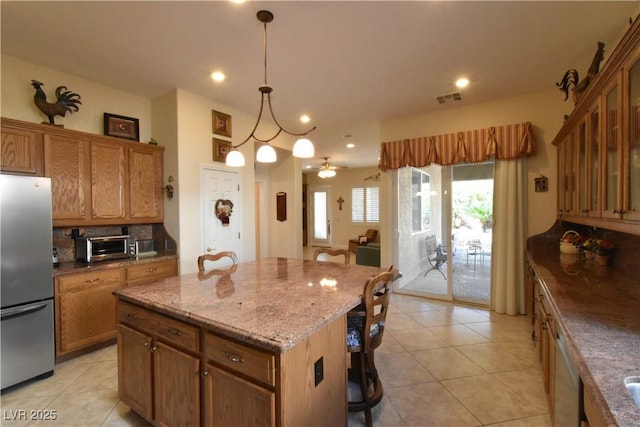 kitchen featuring visible vents, a kitchen breakfast bar, a center island, freestanding refrigerator, and decorative backsplash