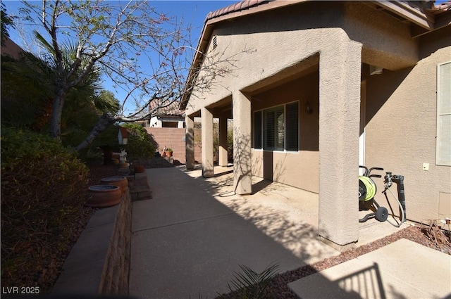 view of side of property featuring stucco siding, a tiled roof, a patio, and fence