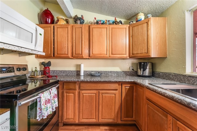 kitchen with white microwave, lofted ceiling, stainless steel range with electric cooktop, a textured ceiling, and a textured wall