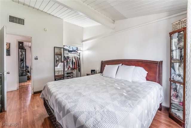 bedroom featuring lofted ceiling with beams, visible vents, a closet, and wood finished floors