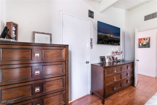 bedroom with beam ceiling, light wood-style flooring, and visible vents