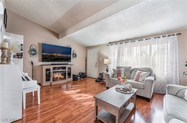 living area featuring lofted ceiling with beams, a textured ceiling, a glass covered fireplace, and light wood finished floors