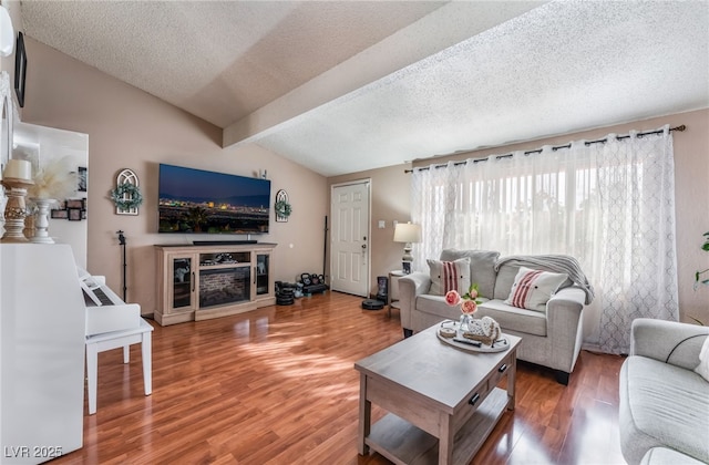 living area featuring light wood-style flooring, a textured ceiling, vaulted ceiling with beams, and a fireplace