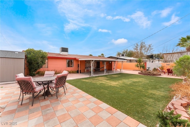 rear view of property with a patio, an outbuilding, fence, a storage unit, and a lawn