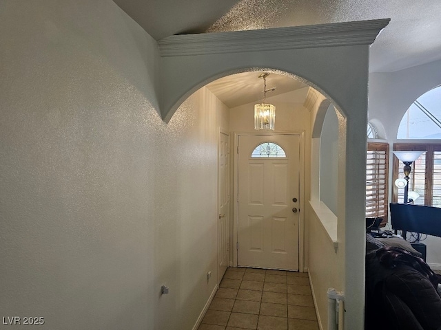 foyer featuring a notable chandelier, lofted ceiling, arched walkways, light tile patterned flooring, and baseboards