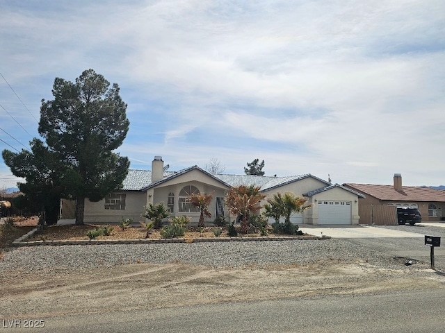 ranch-style house with a chimney, an attached garage, driveway, and stucco siding