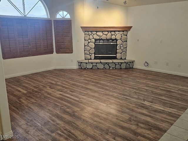 unfurnished living room featuring wood finished floors, baseboards, and a stone fireplace