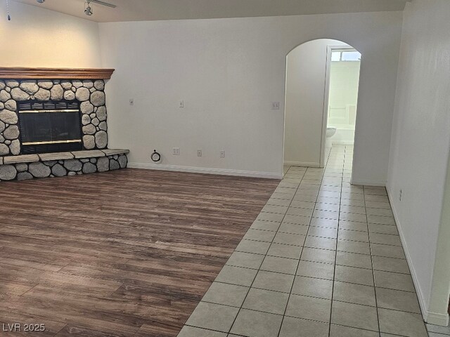 unfurnished living room featuring a stone fireplace, arched walkways, wood finished floors, and baseboards