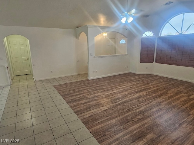 unfurnished room featuring ceiling fan, arched walkways, wood finished floors, and lofted ceiling