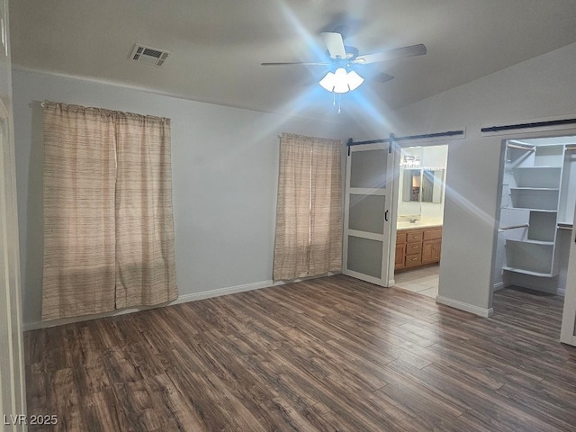unfurnished bedroom with baseboards, connected bathroom, a barn door, visible vents, and wood finished floors