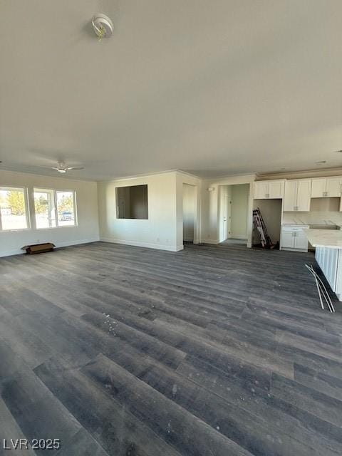 unfurnished living room with dark wood finished floors, baseboards, and ceiling fan