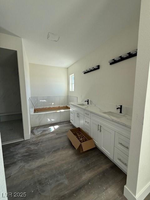 bathroom with a sink, baseboards, a bath, and double vanity