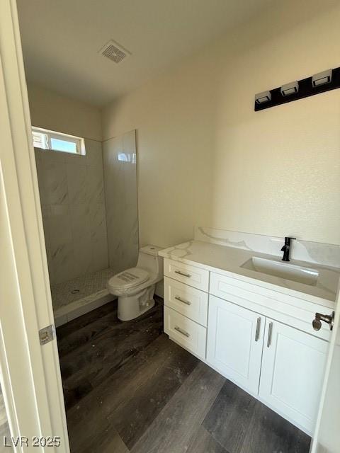full bath featuring vanity, wood finished floors, visible vents, tiled shower, and toilet