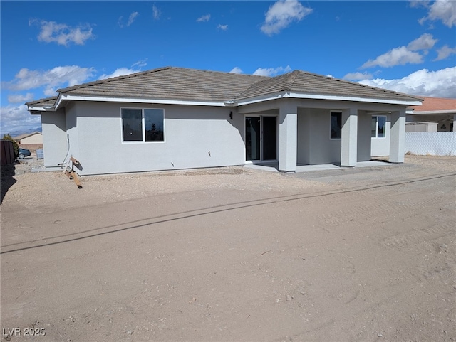 back of property featuring stucco siding, a tile roof, and fence