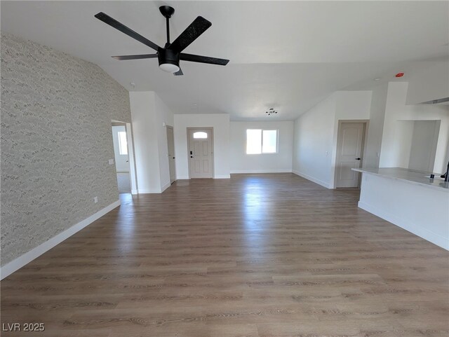 unfurnished living room featuring ceiling fan, baseboards, vaulted ceiling, and wood finished floors
