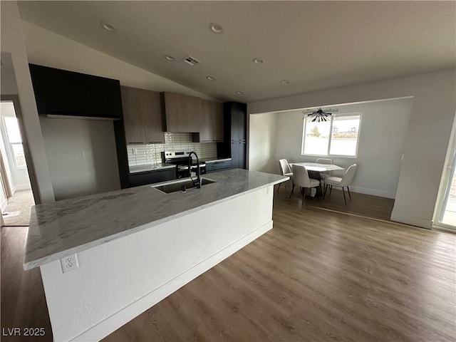 kitchen featuring light wood-type flooring, backsplash, a center island with sink, a sink, and light stone counters
