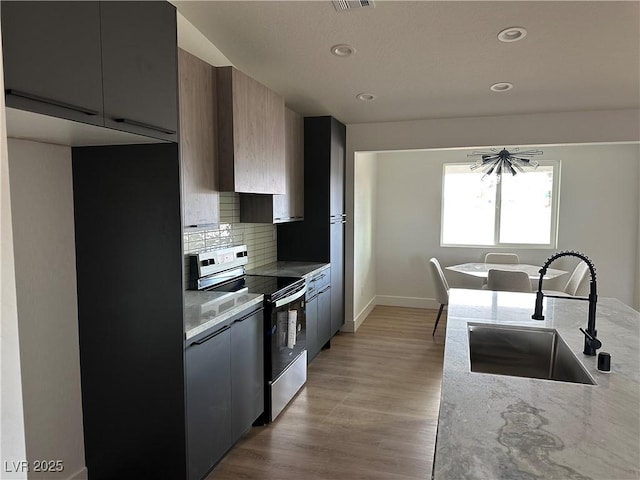 kitchen featuring tasteful backsplash, light wood-type flooring, baseboards, a sink, and electric range oven