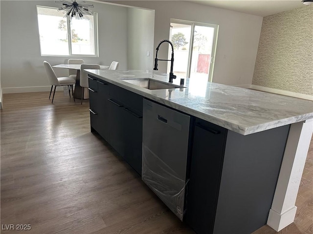 kitchen featuring a sink, light stone countertops, dishwasher, a center island with sink, and light wood-style floors