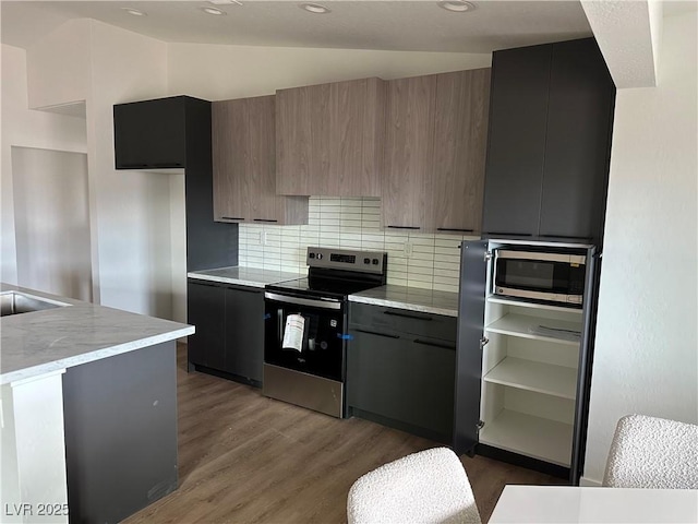 kitchen featuring decorative backsplash, modern cabinets, wood finished floors, stainless steel appliances, and vaulted ceiling