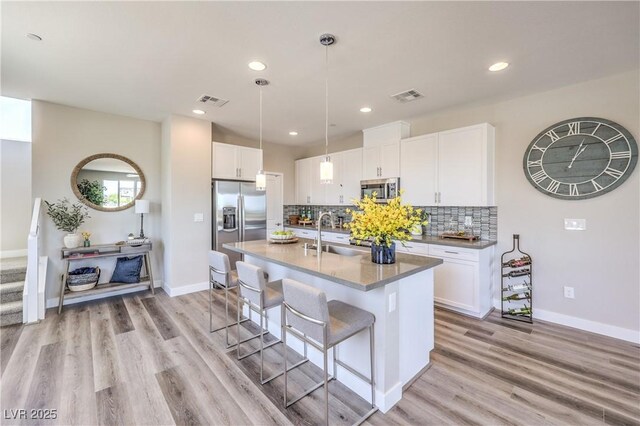8629 Ensworth St Unit 114, Las Vegas, NV 89123 - kitchen with stainless steel appliances, a kitchen bar, white cabinets, decorative backsplash, and light wood-type flooring