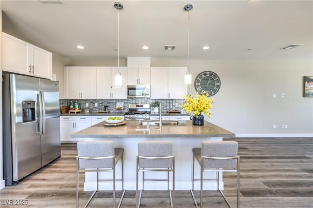 8629 Ensworth St Unit 114, Las Vegas, NV 89123 - kitchen featuring stainless steel appliances, wood finished floors, a breakfast bar, tasteful backsplash, and white cabinetry