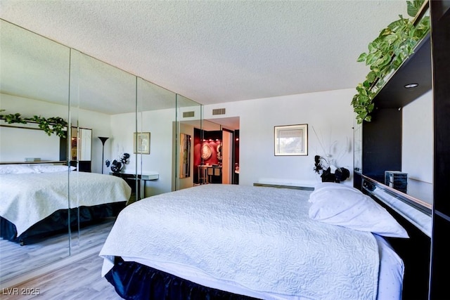 bedroom featuring wood finished floors, visible vents, and a textured ceiling