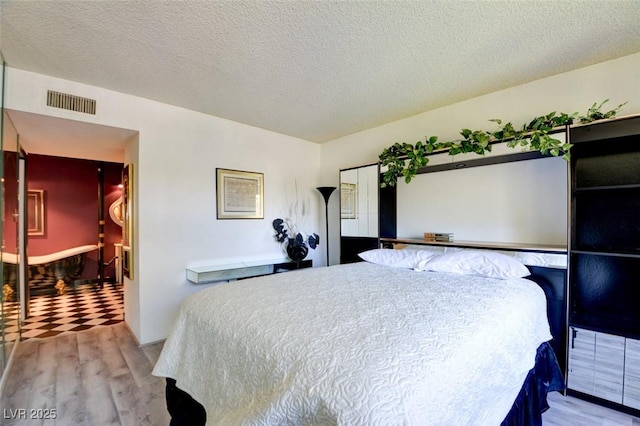 bedroom featuring light wood finished floors, visible vents, and a textured ceiling