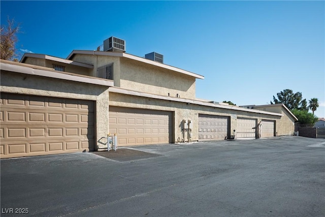 view of side of property featuring community garages, cooling unit, and stucco siding