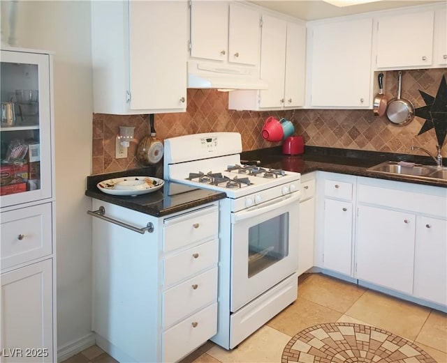 kitchen with dark countertops, white gas range, a sink, backsplash, and under cabinet range hood