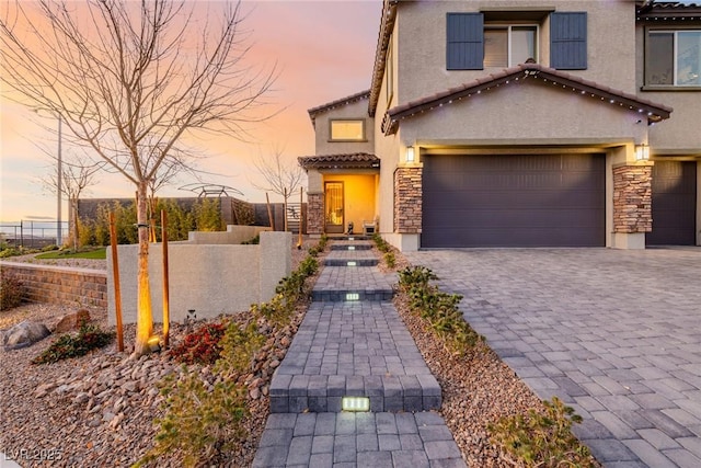 view of front of property with decorative driveway, stone siding, a garage, and stucco siding